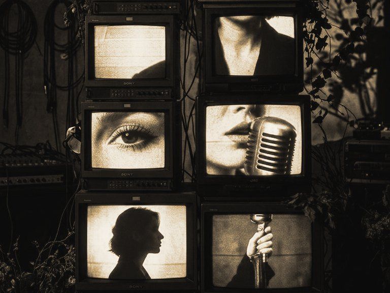 Una cantante al microfono sugli schermi di una torre di televisori a tubo.